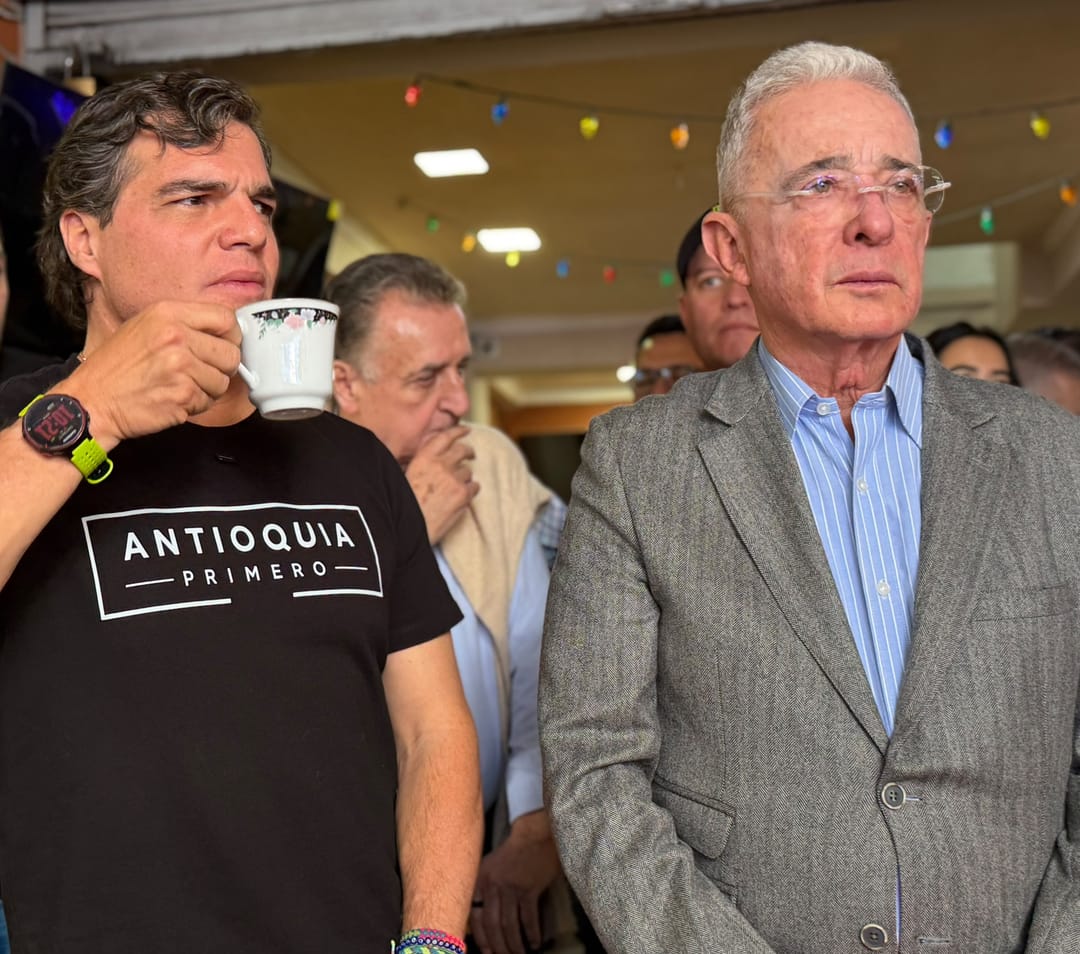 Alejandro Arbeláez A., con camiseta «Antioquia Primero» y un pocillo de café, de pie junto a Álvaro Uribe Vélez